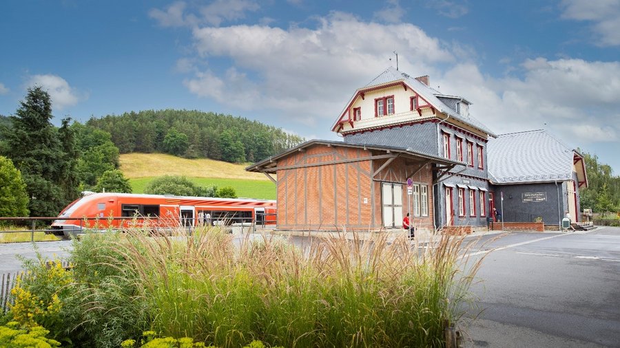 Zug fährt durch Bahnhof in ländlicher Region.